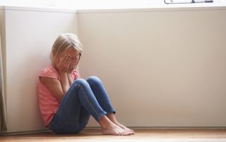 Unhappy Child Sitting On Floor In Corner At Home