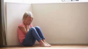 Unhappy Child Sitting On Floor In Corner At Home
