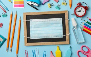 School supplies with medical mask and sanitizer on blue backgrou