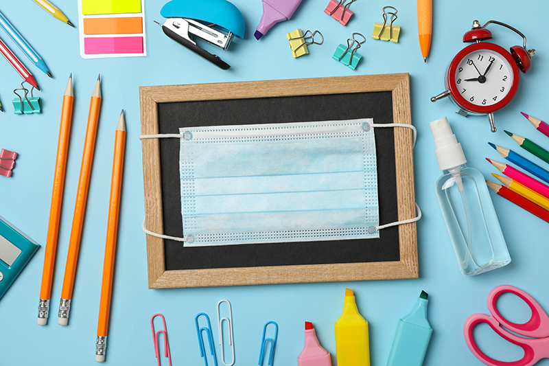 School supplies with medical mask and sanitizer on blue backgrou